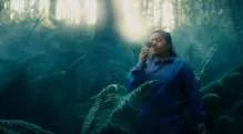 Film still of a woman seated among green forest vegetation